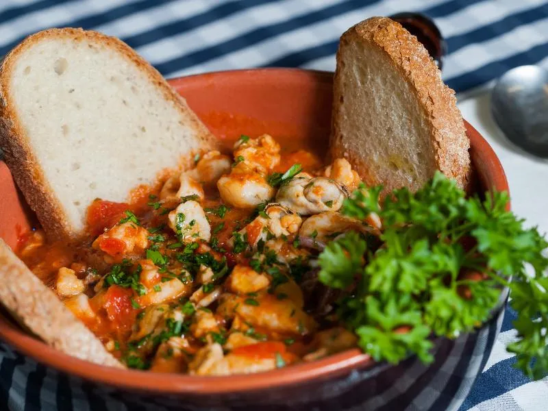 Pieces of fish and shellfish in a red tomato broth, with toasted bread and parsley in a terracotta bowl